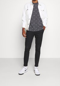 Biała dżinsowa kurtka, paskowana granatowo-biała koszulka z małymi wzorami, czarne spodnie i białe sneakersy z czarnymi akcentami.