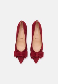 Ballerines en suède rouge avec un bout pointu et de grands nœuds en tissu accentués à l'avant. Doublure intérieure lisse. Semelle durable.