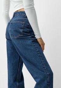 Högmidjade, löst sittande blå denimjeans med två bakfickor, med en texturerad tyg och synliga söm detaljer.