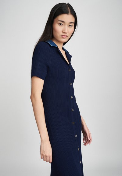 Robe en tricot côtelé bleu marine avec un col en denim, des manches courtes et des boutons dorés sur le devant, avec une silhouette slim et ajustée.