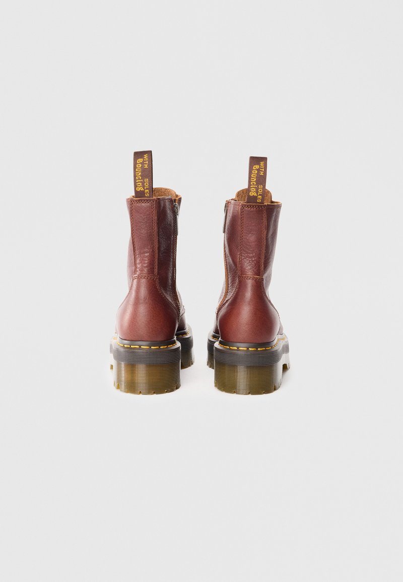 Bottes en cuir marron à la cheville avec une finition texturée, fermeture éclair latérale et une semelle chunky et translucide. Comprend un tirant jaune.