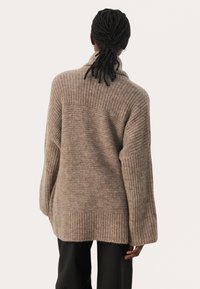 Beige gestrickter Pullover mit geripptem Kragen und Ärmeln, der eine lockere Passform und ein strukturiertes Muster auf der Rückseite aufweist. Lange, weite Ärmel.