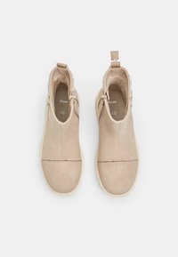 Stivaletti in suede beige con punta arrotondata, cerniere laterali e suola texturizzata. Presenta un design cucito e una linguetta sul tallone per una facile calzata.