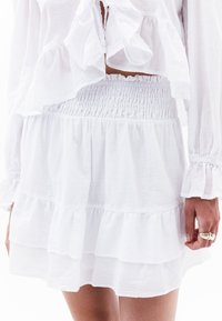 Falda blanca en capas con cintura fruncida y dobladillo ondulado, hecha de una tela ligera. Presenta un patrón texturizado y una caída suave.