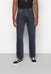 Mörkblå denimjeans med rakt ben, fem fickor och knappstängning. Bärs med svarta sneakers med vita detaljer.