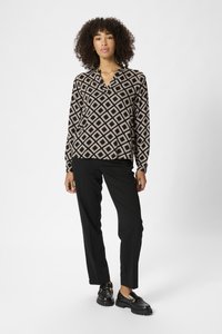 Schwarz-braun gemusterte Bluse mit langen Ärmeln und Notch-Kragen, kombiniert mit schwarzen geraden Hosen und klobigen schwarzen Schuhen.