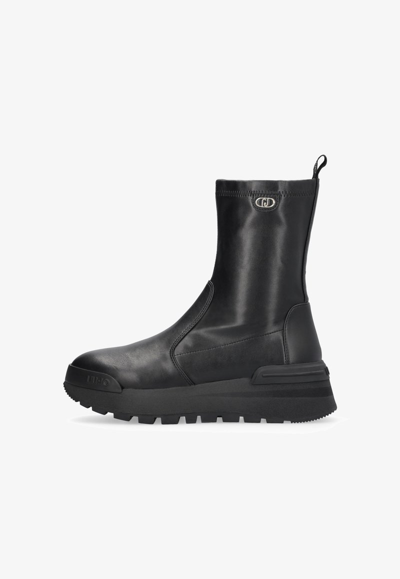 Botte mi-mollet en cuir noir avec semelle épaisse et rainurée, bout arrondi, languette de tirage et emblème logo argenté près du haut.