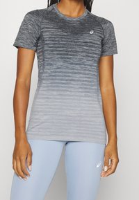 Camiseta deportiva gris con un diseño en degradado, detalles de malla en los hombros, escote redondo y mangas cortas, combinada con leggings de color azul claro.