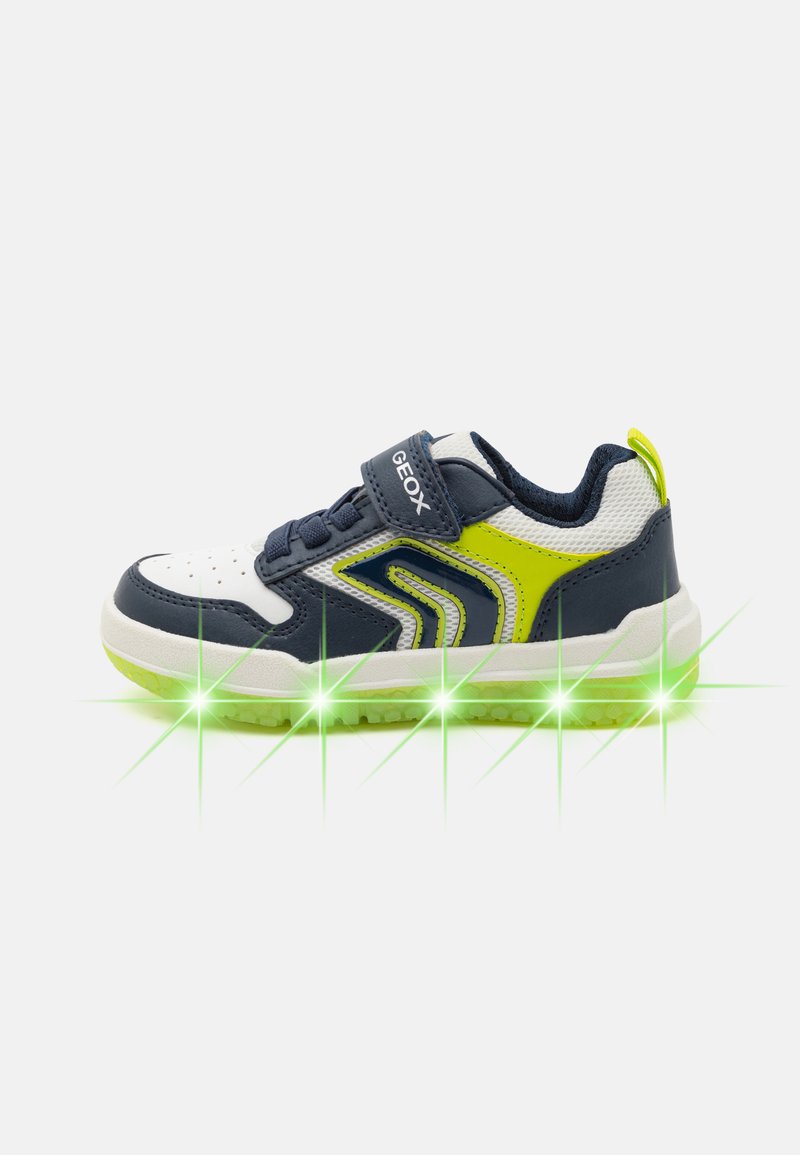 Navy and white sneakers with a green sole, featuring a Velcro strap, mesh upper, and bright yellow accents.  Light accents along the base.