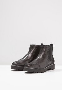 Un par de botines de cuero negro texturizado con paneles laterales elásticos y suelas de goma gruesa sobre una superficie blanca.