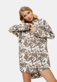 Brązowa i biała sukienka koszulowa z wzorem w plamki bydła, z długimi rękawami i luźnym krojem, z kołnierzykiem.