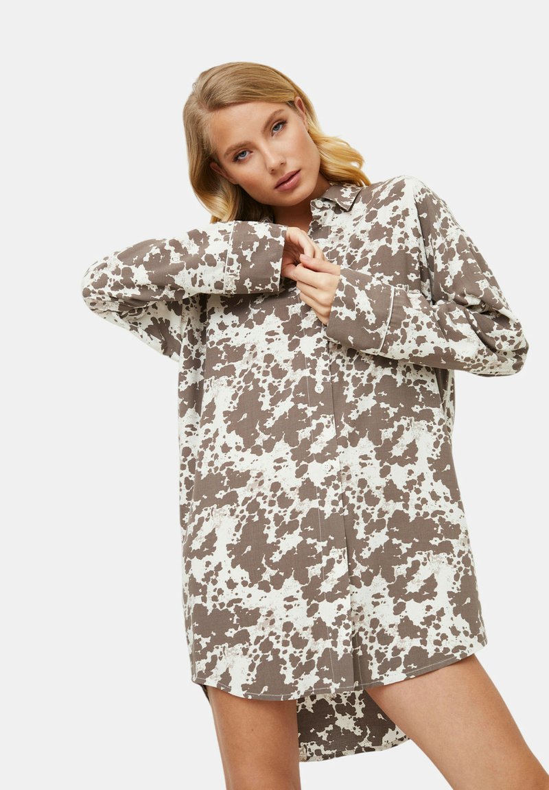 Brązowa i biała sukienka koszulowa z wzorem w plamki bydła, z długimi rękawami i luźnym krojem, z kołnierzykiem.