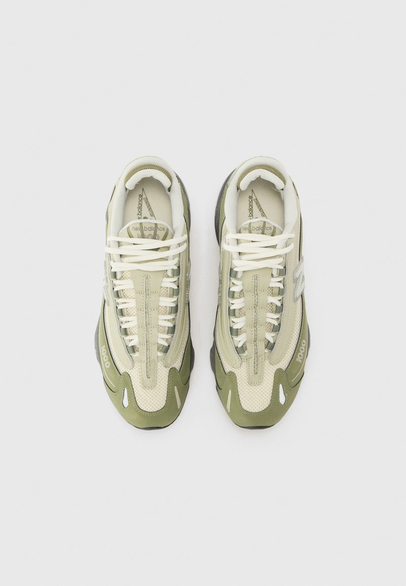 Zapatilla de color claro con acentos verde oliva, paneles texturizados y cordones blancos. Cuenta con una lengüeta acolchada y suela de goma.