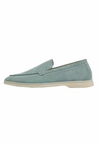 Scarpe slip-on in suede azzurro chiaro con punta arrotondata e suola bassa crema. Presentano un design minimalista e dettagli cuciti lungo la parte superiore.