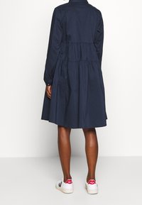 Mörkblå skjortklänning med långa ärmar, samlad midja och utsvängd kjol. Matchas med vita sneakers med röda detaljer.