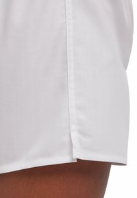 Shorts blancs avec un motif texturé à rayures. Dotés d'un ourlet net et d'une fente latérale pour faciliter les mouvements. Confectionnés dans un tissu léger.