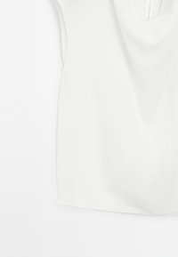 Top blanc sans manches à encolure drapée présenté sur fond blanc, mettant en valeur la texture et les plis du tissu.