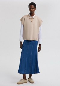 Beige korte mouwen trui met drie bruine knopen, over een wit shirt. Blauwe denim maxi rok, licht tan sneakers, met textuur.