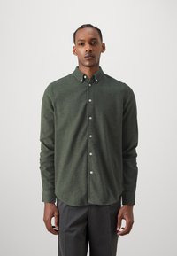 Green button-up shirt made of soft textured fabric, featuring a classic collar and white buttons, paired with gray trousers.