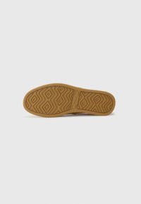 Suela de zapato con un patrón de diamante, hecha de goma marrón. Presenta un contorno suave y el nombre de la marca "TOMS" visible en la superficie.