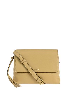 Sac bandoulière en cuir beige avec une sangle ajustable, une fermeture à rabat, de petites clous métalliques sur le devant et un détail de pompon sur le côté.