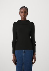 Pull noir côtelé avec un large col replié et des manches longues, associé à une jupe en denim bleu avec une fente à l'avant.