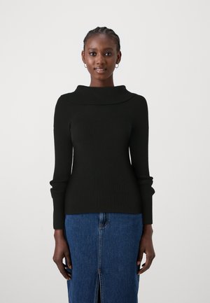 Maglione nero a coste con un ampio colletto ripiegato e maniche lunghe, abbinato a una gonna di denim blu con uno spacco frontale.