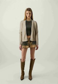Beige strikkearkade over en mørkegrønn cropped topp, kombinert med en brun plissert miniskjørt og brune knelang hæl støvler.