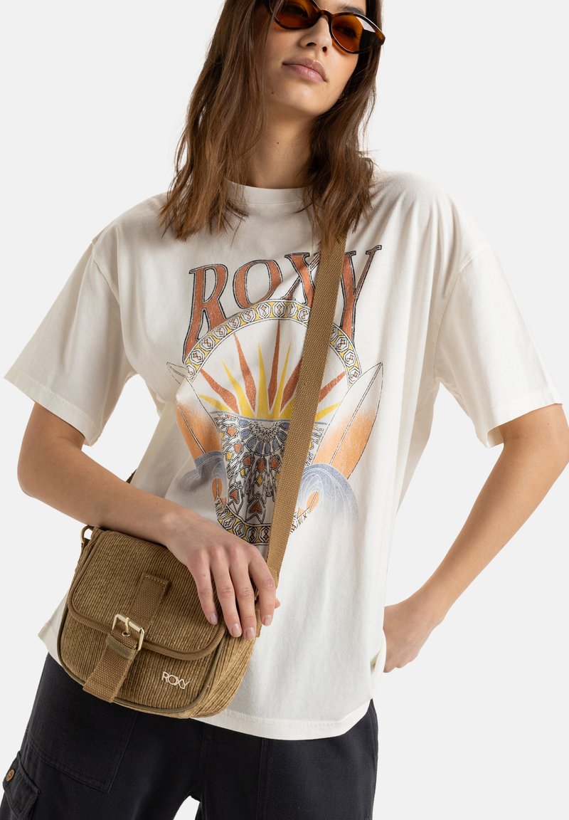 Braune Kord-Tasche mit Umhängegurt, Klappenverschluss und verstellbarem Trageriemen, kombiniert mit einem weißen Grafik-T-Shirt, das bunte Muster zeigt.