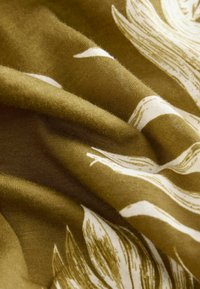 Cotton fabric in olive green with white floral patterns, displaying a soft texture and natural drape, highlighting wavy design elements.