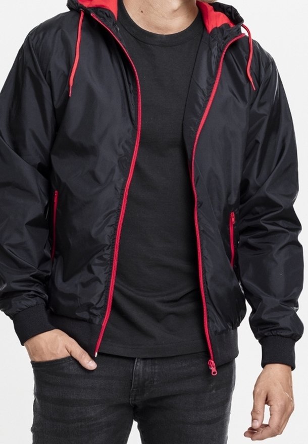 Schwarze Nylonjacke mit rotem Innenfutter und Reißverschlüssen. Verfügt über eine Kapuze, elastische Bündchen und Seitentaschen. Glatte Textur und leichtes Design.