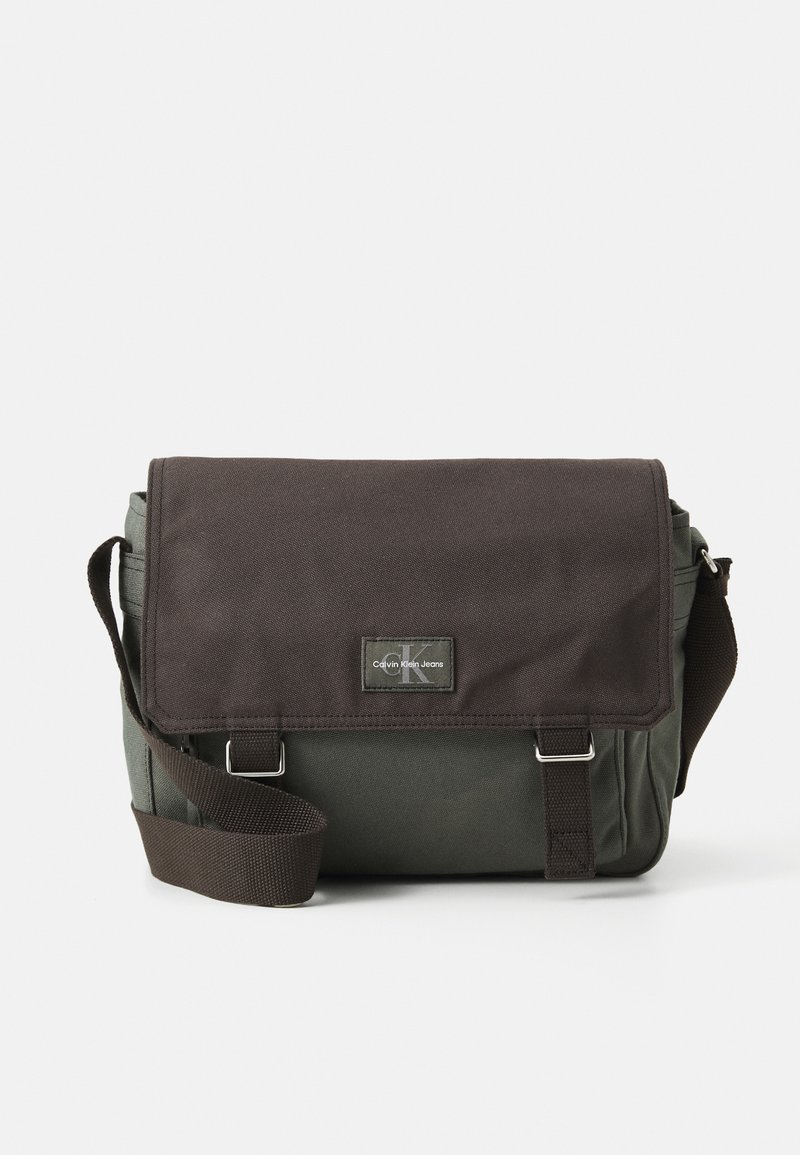 Borsa a tracolla rettangolare realizzata in tessuto resistente, con un flap marrone scuro, corpo verde, tracolla regolabile e una toppa con il logo.