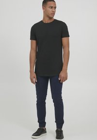 Svart t-skjorte med korte ermer kombinert med marineblå slim-fit cargo-bukser, med sidelommer, og svarte joggesko med hvit såle.