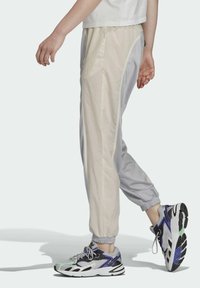 Gaiši krēmkrāsas un gaiši pelēki viegli sporta bikses ar elastīgām aprocēm un sānu joslām. Kombinētas ar daudzkrāsainiem sporta apaviem.