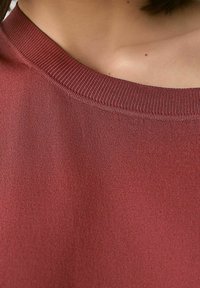 Pull en bordeaux avec un col en côtes, une texture douce, un design ajusté et un tissu lisse, présentant des coutures régulières et peu de détails.