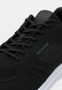 Černá sportovní bota s pěnovou vrchní částí, texturovanými detaily, tonálními tkaničkami a značkovou patní částí. Bílá podešev jako kontrast.