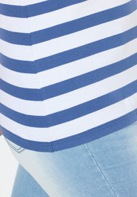 Camicia a righe in cotone blu e bianco, con scollo a girocollo e orlo a costine. Abbinata a jeans in denim azzurro chiaro.