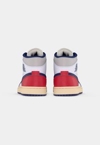 Sneakers alte in pelle bianca, con accenti rossi e blu navy, colli imbottiti e suola in gomma testurizzata. Presentano un logo ricamato sul lato.