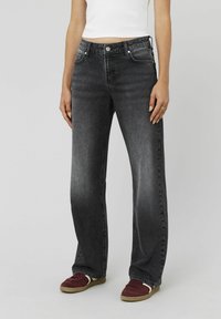 Jeans en denim noir avec une coupe droite, dotés de poches avant, d'un style classique à cinq poches et d'une légère décoloration sur le tissu.