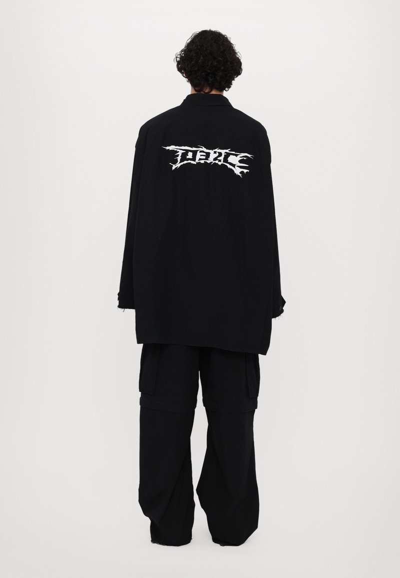 Camisa negra de gran tamaño con gráfico blanco "FIERCE" en la parte posterior, combinada con pantalones cargo negros holgados. Material de algodón, corte relajado.