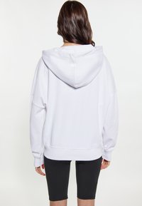 Felpa bianca oversize con cappuccio ampio e maniche larghe, abbinata a pantaloni corti neri. Tessuto morbido con una superficie liscia e senza motivi visibili.