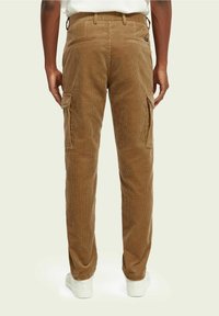 Marron corduroy cargo-housut, joissa on useita taskuja, ribbed-rakenne ja suora malli. Valkoiset lenkkarit näkyvät alhaalla.