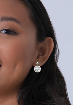 Boucles d'oreilles en argent avec une tige sphérique et un pendentif rond présentant un design texturé et en relief, mettant en valeur des détails de motif complexes.