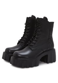 Une paire de bottes en cuir noir à plateforme avec des semelles épaisses à nervures, des lacets à l'avant et des détails rembourrés cousus à l'arrière.