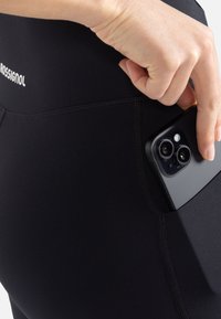 Czarne legginsy zawierają boczną kieszeń zaprojektowaną do przechowywania smartfona. Materiał jest gładki, a krój dopasowany, co czyni je idealnymi do aktywności.