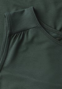 Mörkgrön, slät tyg med en skräddarsydd design. Har en samlad textur vid axelsömmen och en prydlig sydd finish.