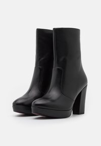 Botines de cuero negro hasta el tobillo con tacones altos en bloque, puntas redondeadas y un acabado suave, con costuras laterales y un diseño de plataforma.
