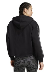 Felpa nera corta con cappuccio, caratterizzata da dettagli neri decorati sulle maniche e un tessuto morbido e strutturato. Abbinata a leggings decorati.