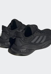 Czarne buty sportowe z przewiewną siateczką, teksturowaną gumową podeszwą oraz wyraźnymi bocznymi paskami. Amortyzowany zapiętek dla wsparcia.