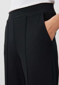 Pantaloni neri su misura in tessuto testurizzato, dotati di tasche frontali e cuciture pinces, che offrono una silhouette strutturata e moderna.